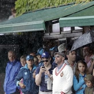 Tennis fans shelter under an awning on Centre Court during a rain delay at the All England Lawn Tennis Club in Wimbledon, London at the 2012 Summer Olympics, Sunday, July 29, 2012. (AP Photo/Elise Amendola)