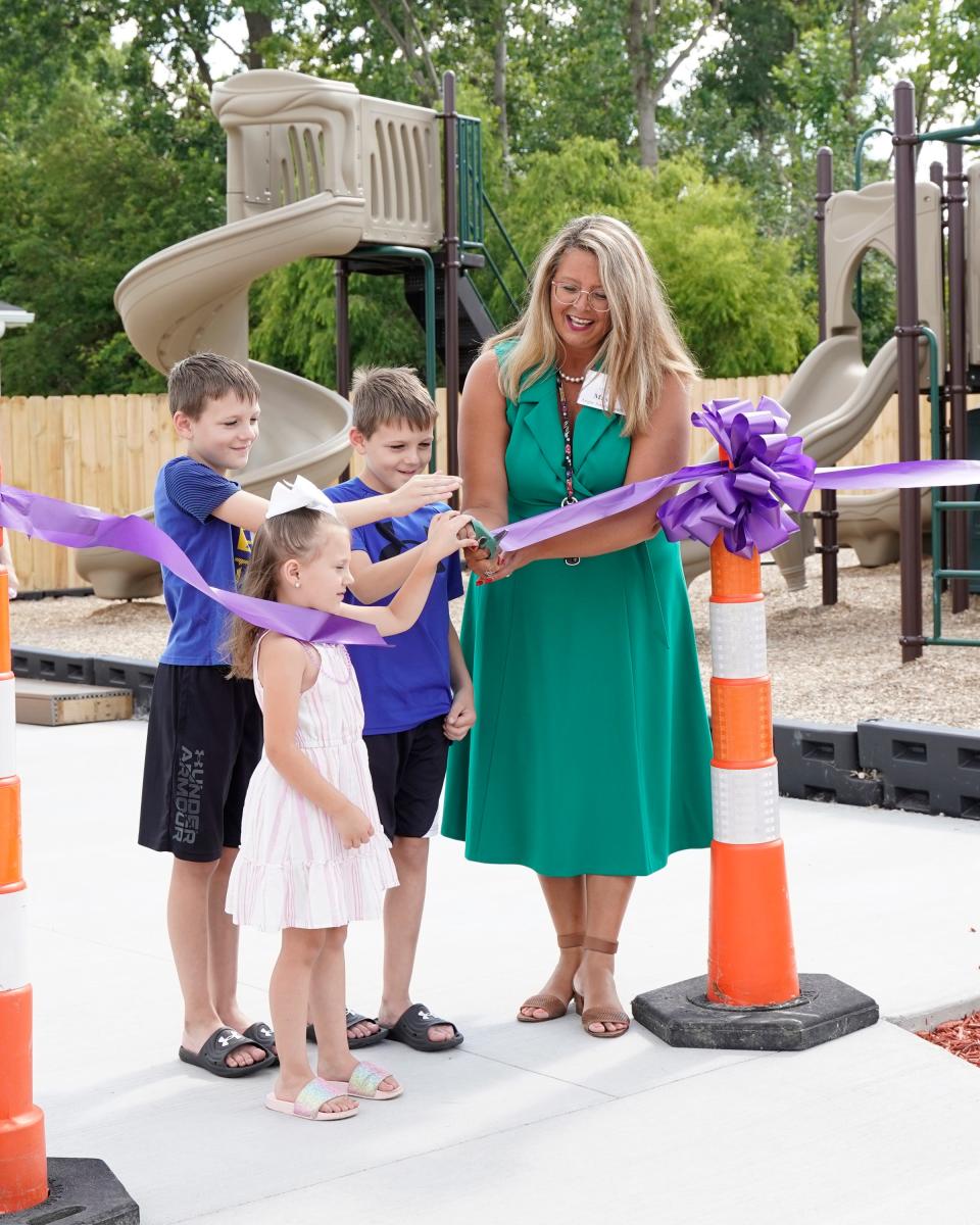 Adrian mayor Angie Sword Heath, right, is assisted during a ribbon cutting event Thursday by twins, Landon and Bentley Wilder, both 8, and younger sister CJ Wilder, 4, at Hidden River North in Adrian. The ribbon cutting was for the mobile home community's newly installed playground, seen in the background.