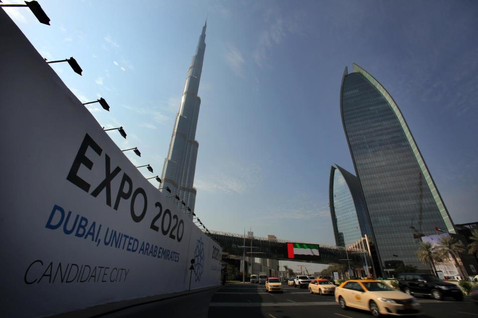 In this Wednesday Nov. 20, 2013, with the Burj Khalifa, the world's tallest building in the background, vehicles pass by a billboard advertising Dubai as a candidate city for the Expo 2020 in Dubai, United Arab Emirates. The logo for Dubai’s bid to host the Expo 2020 reflects a push by the city’s leaders to avert another financial crisis like the one that brought the city to its knees in 2008. Dubai saw property values slashed by more than half and the city’s government needed a $10 billion bailout from oil-rich neighbor Abu Dhabi in 2009. (AP Photo/Kamran Jebreili)