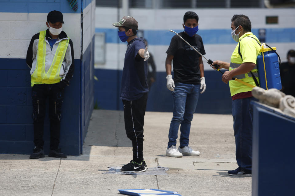 A man is disinfected by a health worker at the site where Guatemalans returned from the U.S. are being held in Guatemala City, Friday, April 17, 2020. Recently deported Guatemalans were placed in a athletic dorm facility to wait for the results of their tests for the new coronavirus. (AP Photo/Moises Castillo)