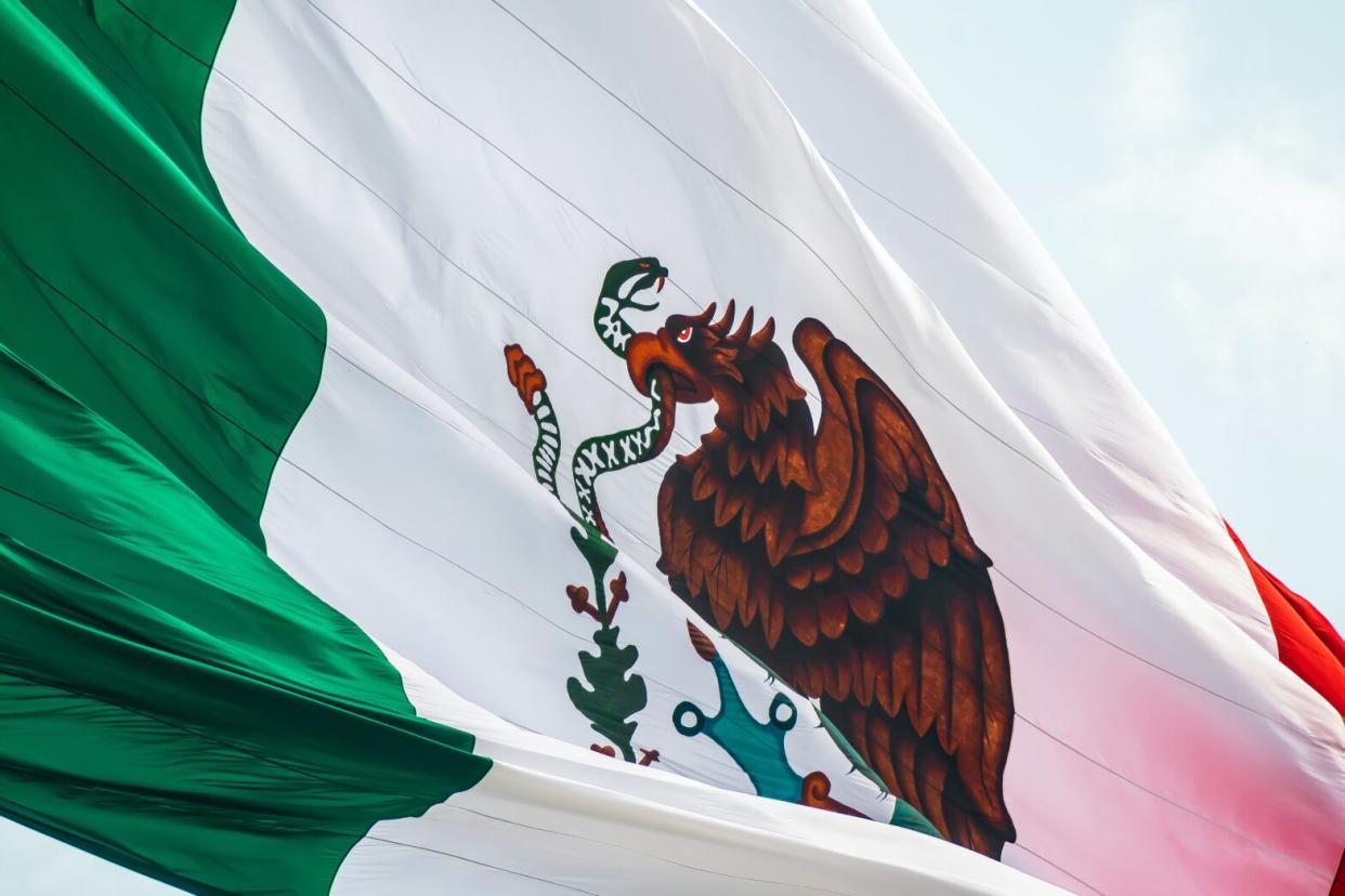 Check out the safest cities in Mexico, which are perfect for a getaway. Pictured: the Mexican flag in front of clouds