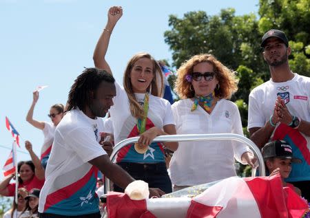 Tennis player and gold medallist Monica Puig (2nd L) greets the crowd while riding on a bus with wrestler Jaime Espinal (L), President of the Olympic Committee of Puerto Rico Sara Rosario (2nd R) and athlete Javier Culson during a welcome ceremony in San Juan, Puerto Rico, August 23, 2016. REUTERS/Alvin Baez