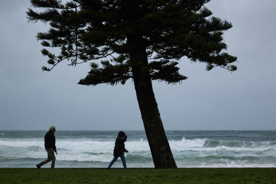 People walk in strong winds and rainy conditions at Manly Beach.