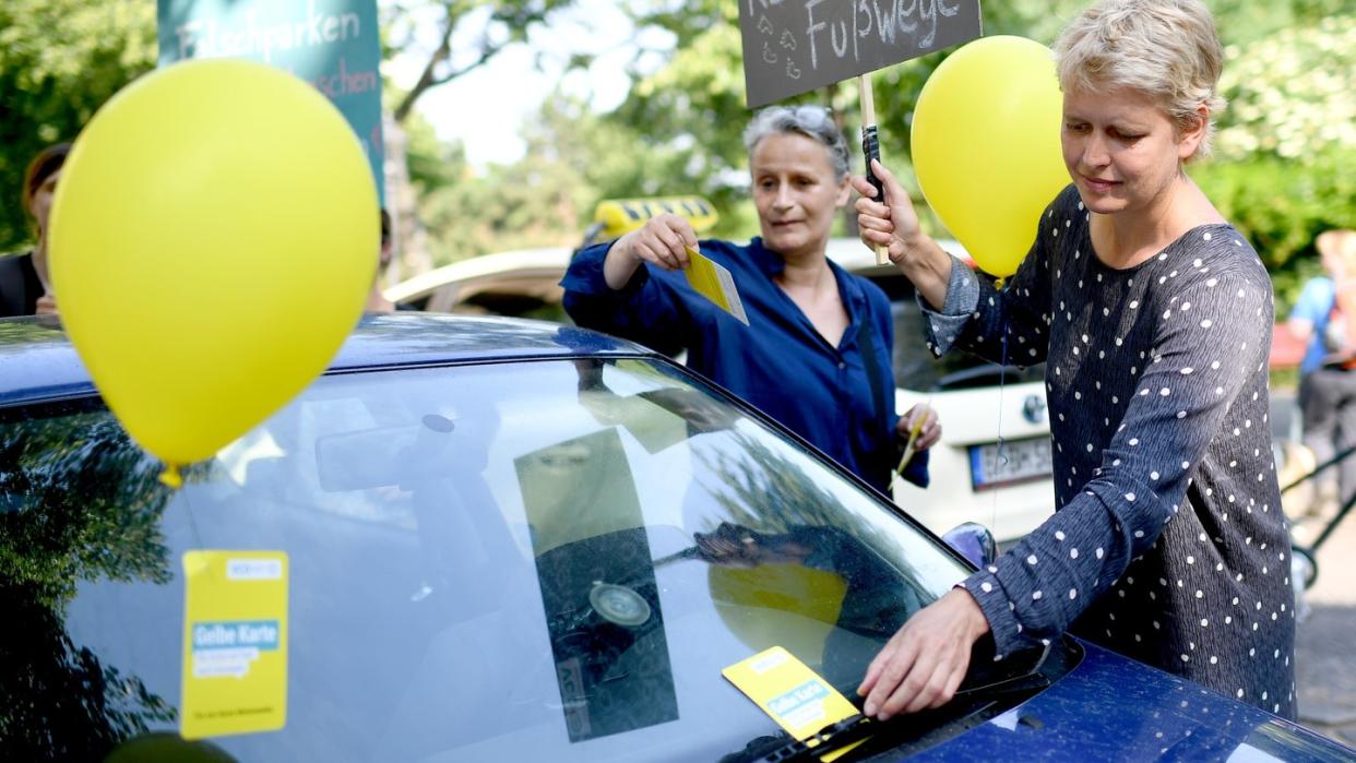 Aktivistin Almut Gaude (r.) heftet einem Auto, dass auf einem Fußgängerübergang geparkt wurde, eine «Gelbe Karte» an. Foto: Britta Pedersen