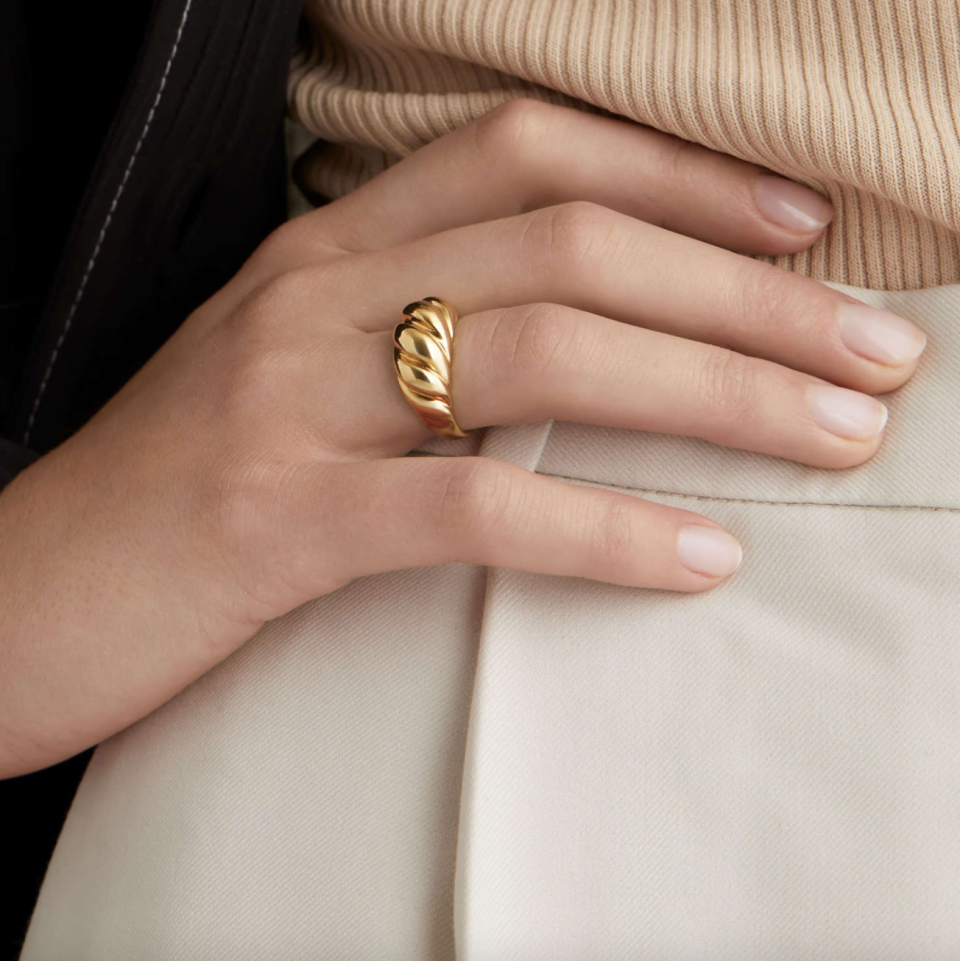 gold Mejuri Croissant Dôme Ring on white woman's hand and white pants