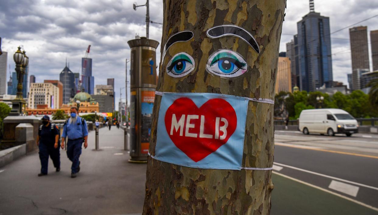 People walk past a tree decorated with eyes and a face mask in Melbourne's central business district on October 15, 2020, as Australia's unemployment rate ticks up to 6.9 percent. (Photo by William WEST / AFP) (Photo by WILLIAM WEST/AFP via Getty Images)