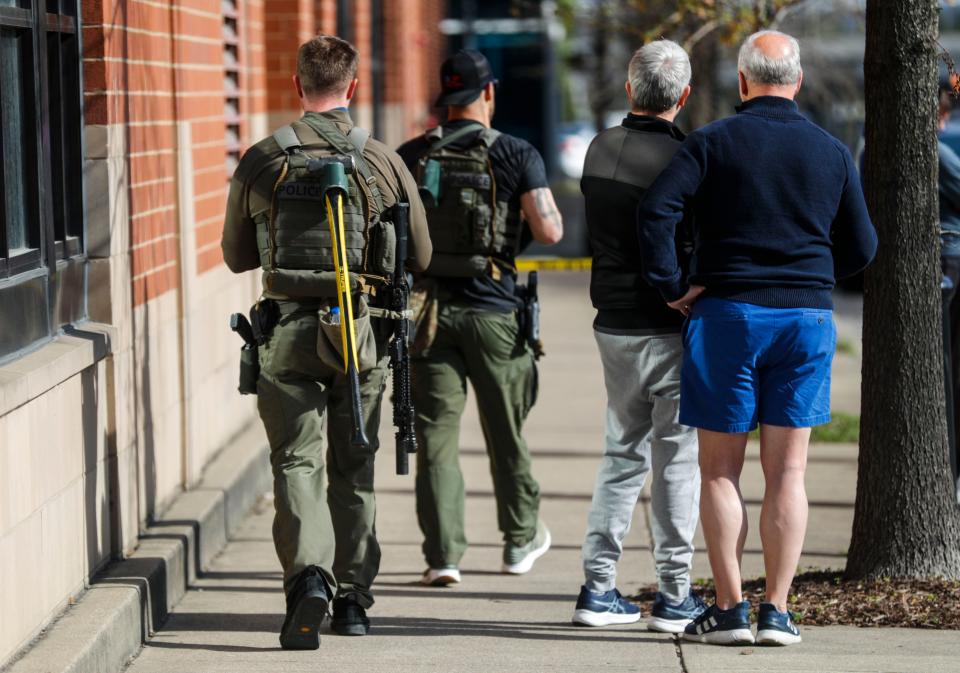 Two LMPD officers walk past bystanders on Preston Street. Five people were shot and killed and six injured, including a LMPD officer, in a deadly Monday morning shooting in downtown Louisville. April 9, 2023