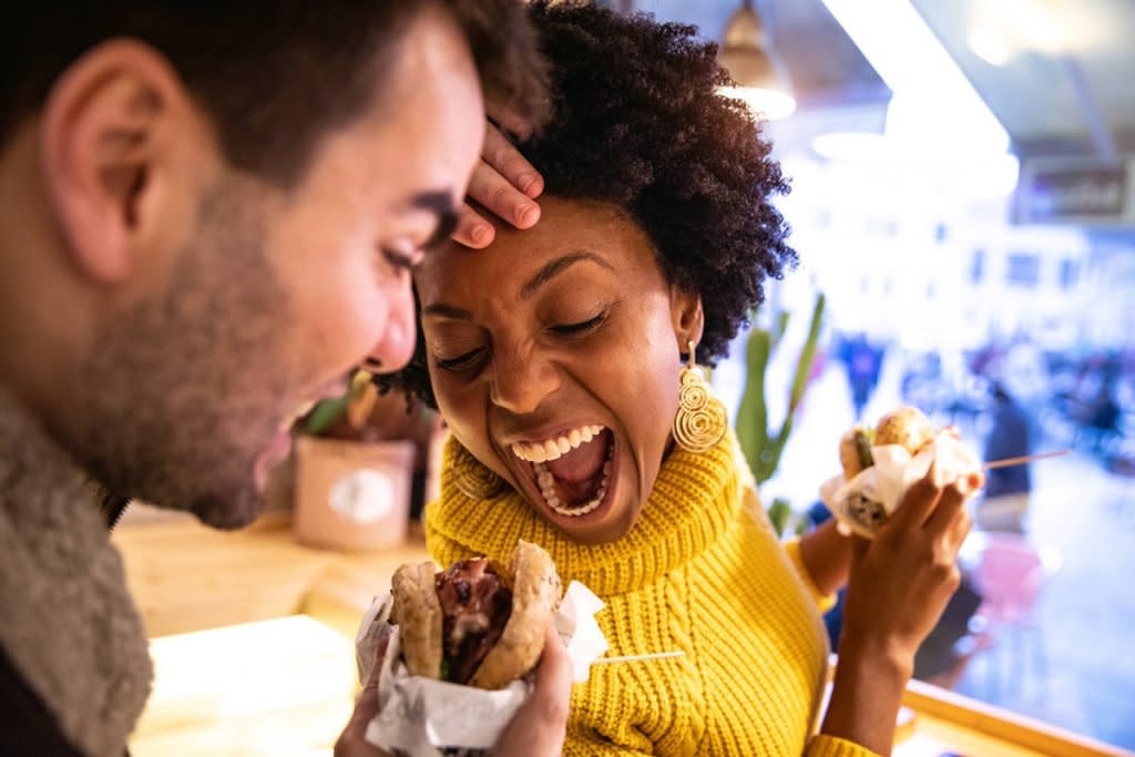 Two people try to take bites out of each other's burgers. 