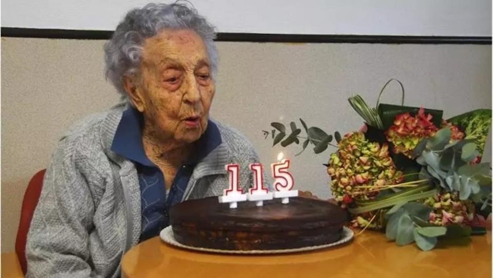 An elderly woman blows out birthday candles.