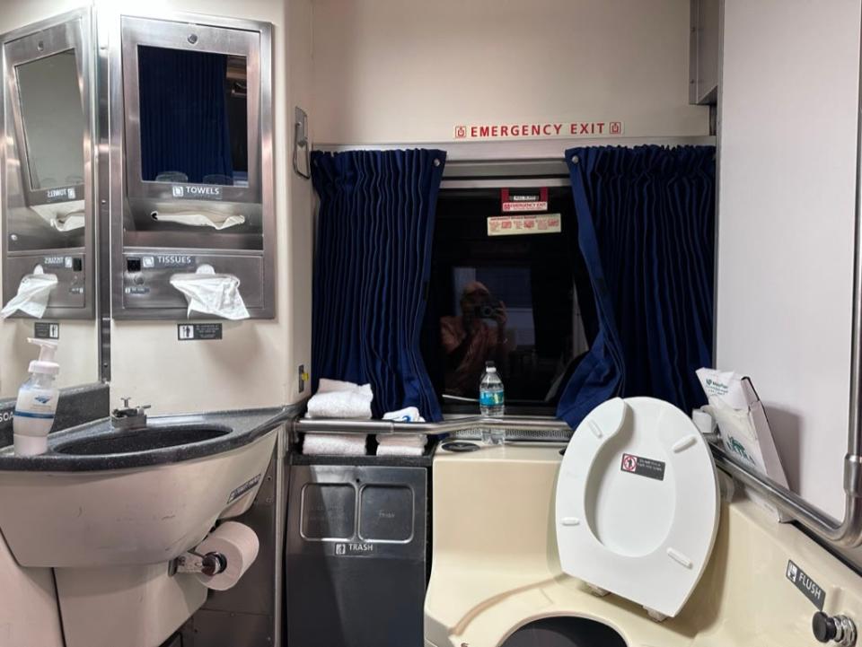 A bathroom on an Amtrak train with a toilet, sink, and trash.