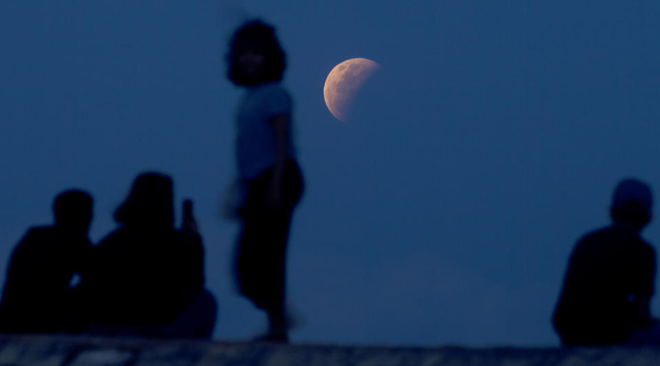 Residents watch the lunar eclipse at Sanur beach in Bali, Indonesia on Wednesday, May 26, 2021. The total lunar eclipse, also known as a super blood moon, is the first in two years with the reddish-orange color the result of all the sunrises and sunsets in Earth's atmosphere projected onto the surface of the eclipsed moon. (AP Photo/Firdia Lisnawati)