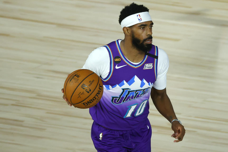 Mike Conley in a purple jersey that says "Jazz" and holding a basketball.