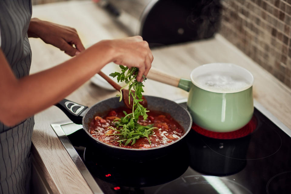 A woman adding arugula to a sauce.