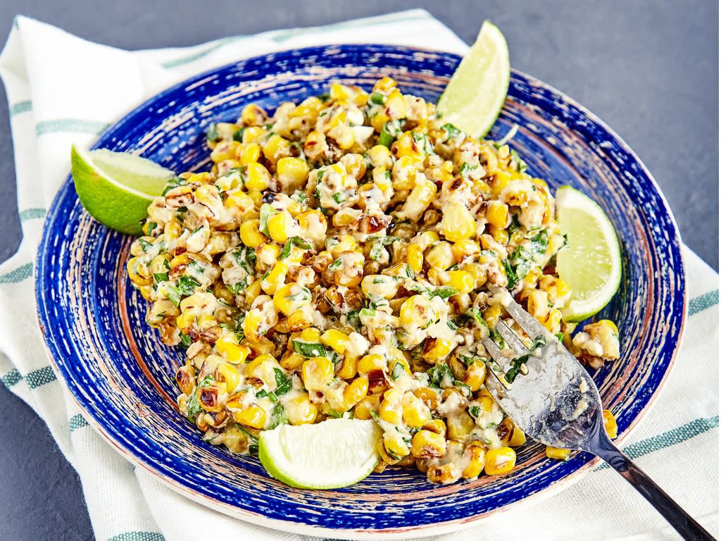 Homemade vegetarian mexican street food corn salad with cilantro, lime, mayonnaise, garlic, chili and cheese on blue vintage plate on stone background. Sweet, sour and hot tastes from mexican cuisine