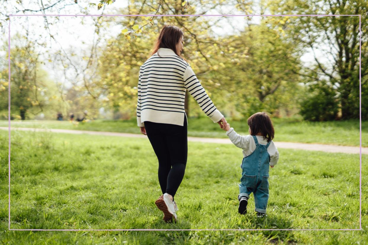  A woman and toddler holding hands while walking through a field. 