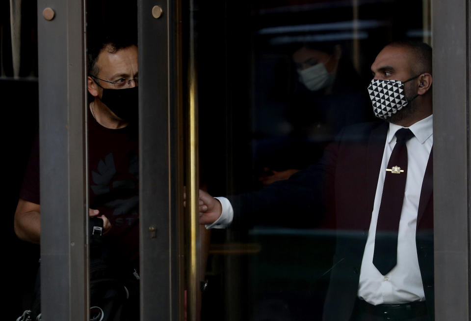 A staff member of a retail store wears a face mask as he opens the door for a client in London, Tuesday, Sept. 22, 2020. British Prime Minister Boris Johnson has slammed the brakes on the country's return to offices, saying people should work from home if possible to help slow the spread of the coronavirus. Johnson on Tuesday announced a package of new restrictions, including a requirement for pubs, restaurants and other hospitality venues in England to close between 10 p.m. and 5 a.m. (AP Photo/Frank Augstein)