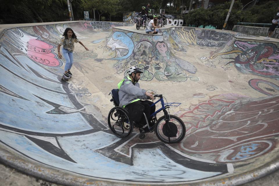 Martin Londoño, right, owner of MATT, an electric wheelchair tour company, rides his wheelchair at a skate park in Medellin, Colombia, Wednesday, Nov. 18, 2020. Londoño says he is trying to promote his tour on social media while building partnerships with local travel companies. He dreams of taking the wheelchair tours to other cities in Colombia, Latin America and the United States. (AP Photo/Fernando Vergara)