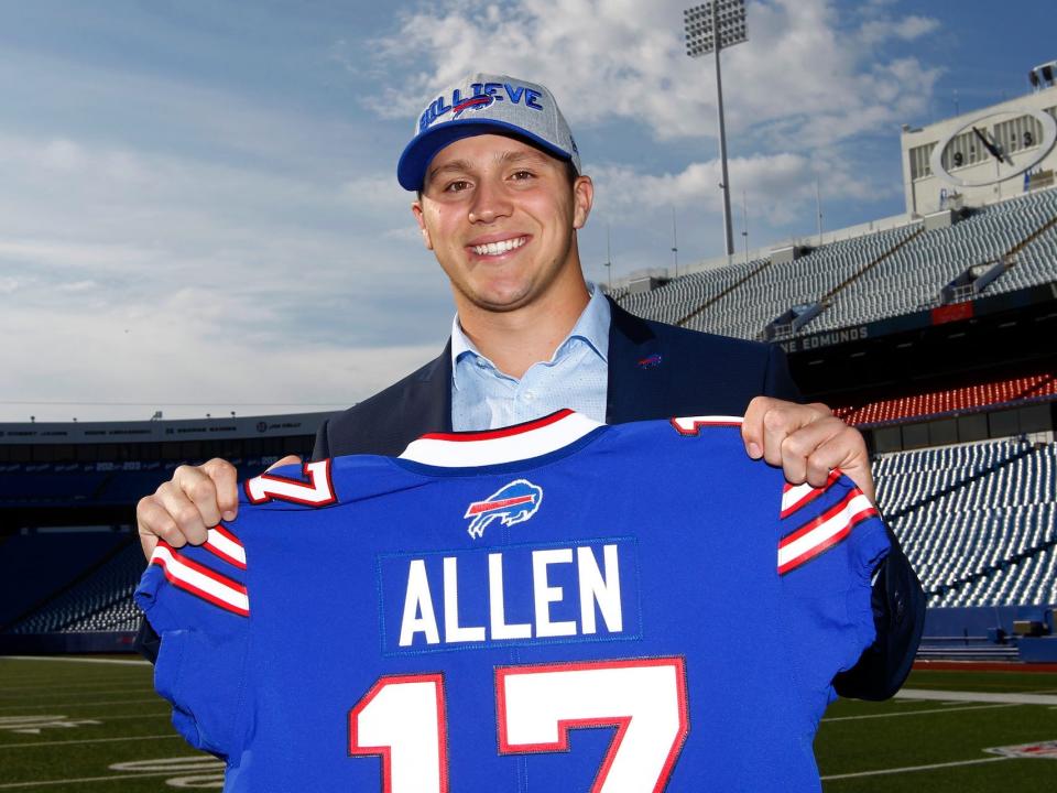 Josh Allen poses with his Bills jersey while standing on the field in an empty stadium in 2018.