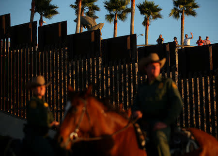 People in Mexico wave at U.S. Border Patrol agents on horseback patrolling the U.S.-Mexico border fence near San Diego, California, U.S., November 10, 2016. REUTERS/Mike Blake