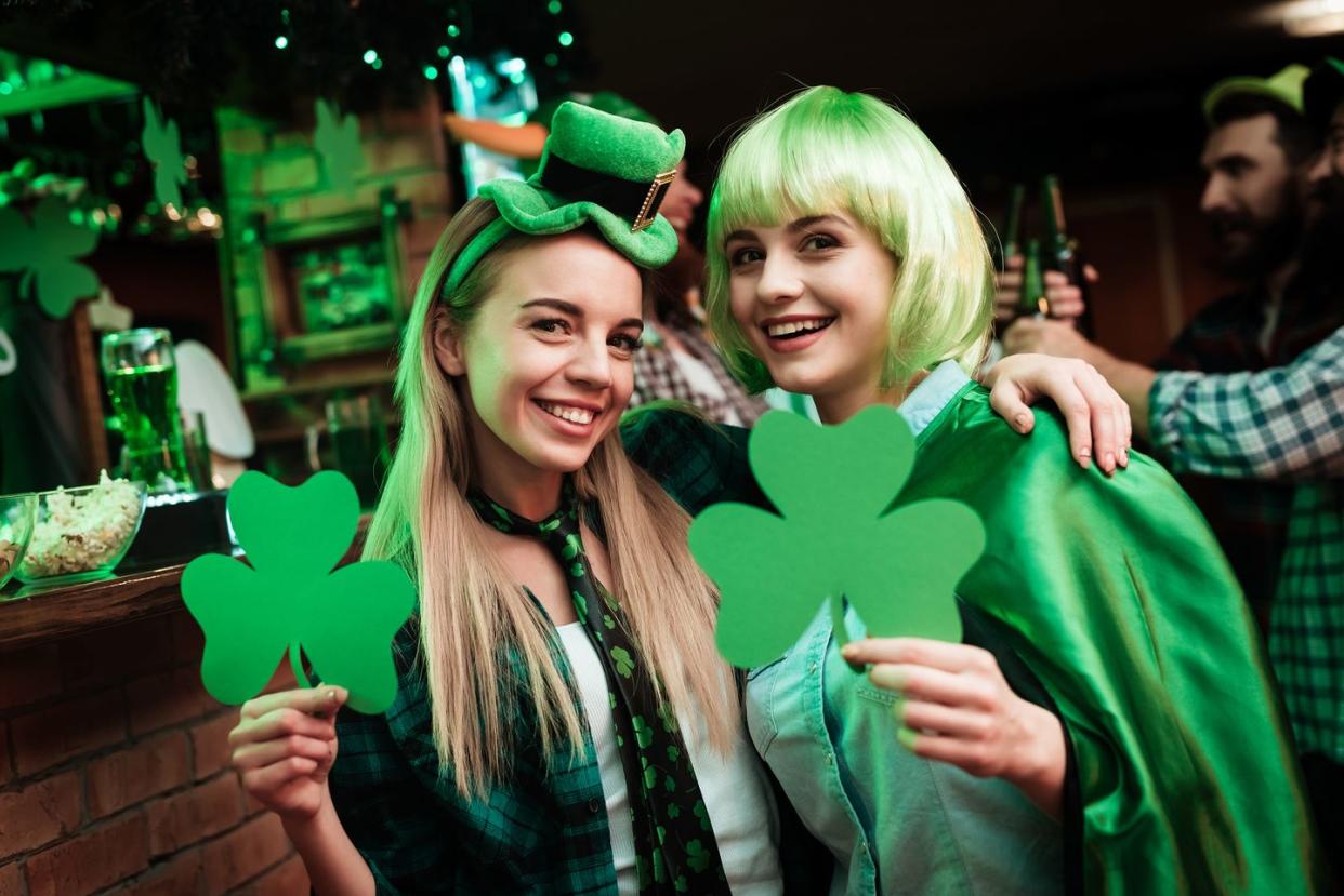 two girls in a wig and a cap are photographed in a bar they celebrate st patricks day they are having fun one girl is holding a clover