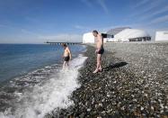 Men wade into the sea on a sunny day as the Olympic Park is seen in the background, during the 2014 Winter Olympic Games in Sochi February 12, 2014. REUTERS/Shamil Zhumatov