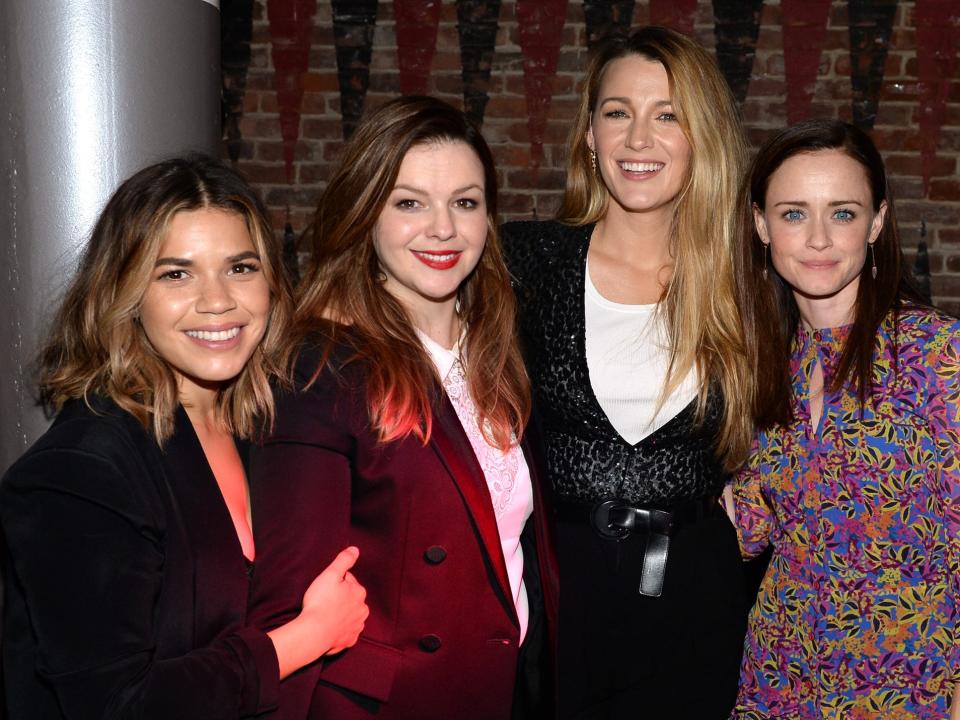 The four friends smiling and embracing each other in blazers and dresses.