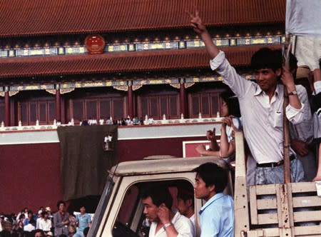 A demonstrator gives the victory sign as workmen finish putting a drape over a huge portrait of Chairman Mao on the Gate of Heavenly Peace in Tiananmen Square in Beijing