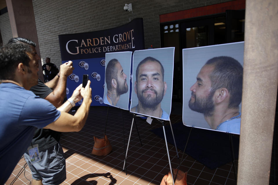 Members of the media take photographs of booking mug shots of Zachary Castaneda posted outside of the Garden Grove Police Department headquarters in Garden Grove, Calif., Thursday, Aug. 8, 2019. Investigators believe Castaneda, a documented gang member, stabbed several people to death and wounded a few others as he targeted his victims at random during a bloody rampage across two Southern California cities, authorities said. (AP Photo/Marcio Jose Sanchez)