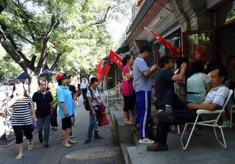 Residents gather outside a shop in Beijing on September 3, 2015 to watch a TV broadcast of the military parade from Tiananmen Square marking the 70th anniversary of victory over Japan and the end of World War II