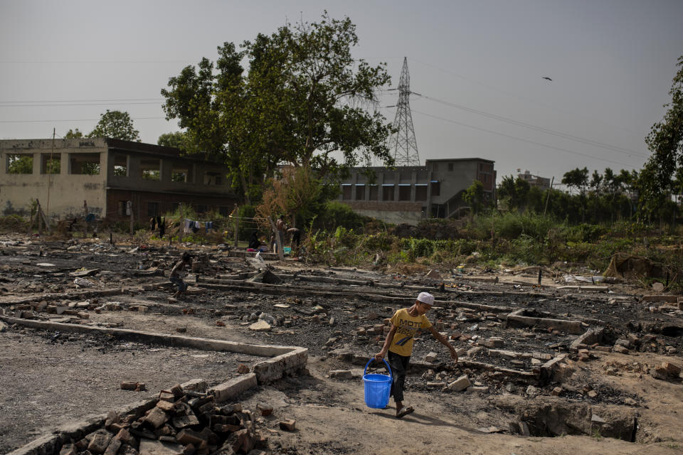 A young Rohingya refugee boy carries a bucket of water through the charred remains of the slum they lived in earlier near a refugee camp alongside the banks of the Yamuna River in the south-eastern borders of New Delhi, sprawling Indian capital, July 1, 2021. Millions of refugees living in crowded camps are waiting for their COVID-19 vaccines. For months, the World Health Organization urged countries to prioritize immunizing refugees, placing them in the second priority group for at-risk people, alongside those with serious health conditions. (AP Photo/Altaf Qadri)