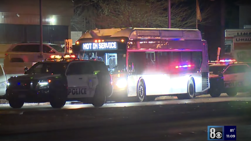 A Las Vegas bust sits stopped with a Not In Service sign on the front. Two police cars stand in front of and behind the bus with their lights on.