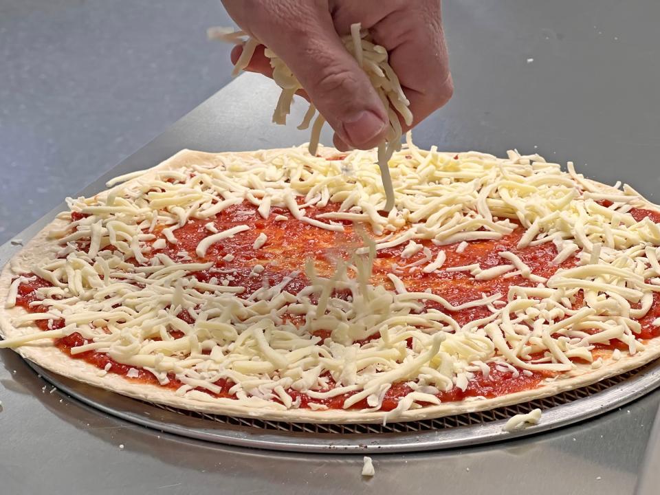 Cheese is sprinkled on a pizza Wednesday afternoon at KD Pizza & Subs on Marion Avenue.