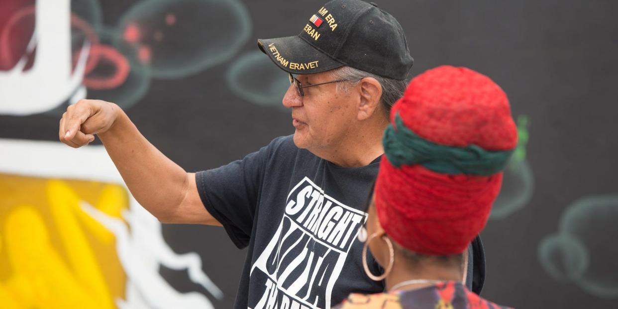 Seneca McIntosh, in a "Straight Outta the Rez" t-shirt, talks to locals in front of the "Black Wall Street" mural in Greenwood.