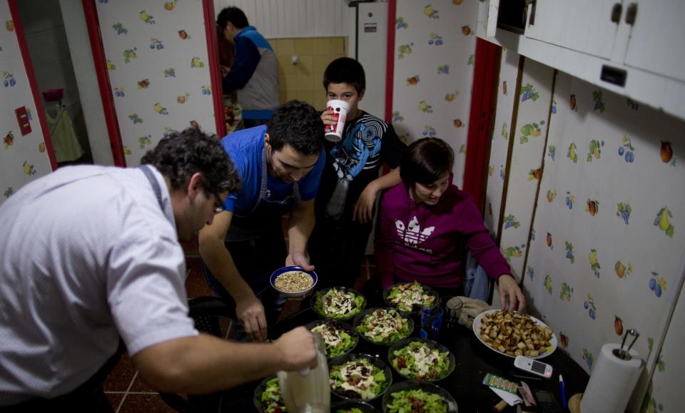 In this April 12, 2014, photo, Chefs Martin Arrojo, left, and Ezequiel De La Torre, second left, Brenda Arrojo, right, prepare salad for customers, as Brenda's son Franco, second right, looks at them while drinking water at their home in Buenos Aires, Argentina. The website www.cookapp.com was launched in March 2013 and recently moved its headquarters from Buenos Aires to New York City. It works like a matchmaker, arranging intimate gourmet dinners between strangers. Chefs list when and where they will prepare particular meals; diners book what interests them, pay upfront via the app, then just show up and enjoy. (AP Photo/Natacha Pisarenko)