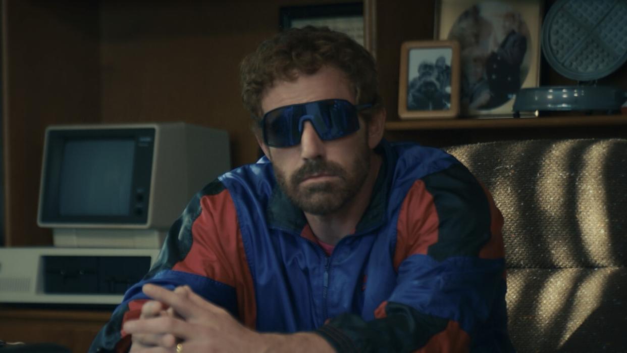  Ben Affleck sits at a desk, wearing shades and a track suit, in Air. 