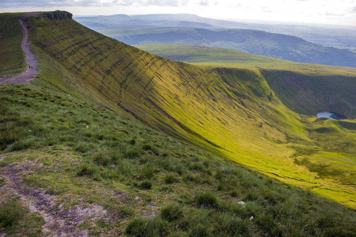 Early evening view along the trail along the ridge between Pen Y Fan and Corn Du in the Brecon Beacons National Park in Powys, Wales, UK. Llyn Cwm Llwch, a glacial mountain lake, can be seen in the valley.