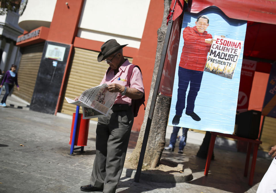 A government supporter reads a newspaper standing next to a poster featuring Venezuela's late President Hugo Chavez with a message that reads in Spanish: "Hot corner, Maduro president," in Caracas, Venezuela, Tuesday, Jan. 29, 2019. “Esquina Caliente” or Hot Corner is a section of Plaza Bolivar where Chavez supporters gather regularly. (AP Photo/Rodrigo Abd)
