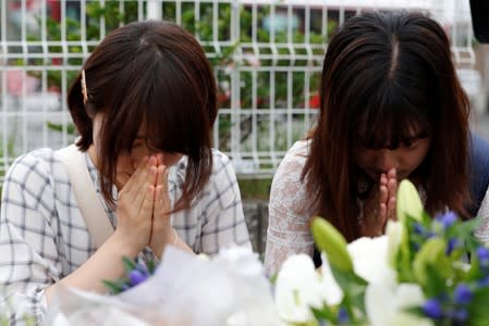 Women pray in front of a row bouquets placed out for victims of the torched Kyoto Animation building in Kyoto