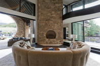 <p>A semi-circular couch fits snugly around a huge open wood burning fireplace constructed of local stone. Massive floor to ceiling windows bring the outside in. </p>