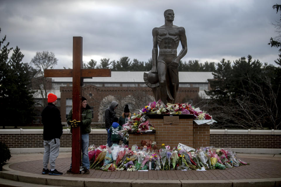 Dan Beazley of Northville Townshipholds a large wooden cross as a crowd gathers at the Spartan Statue, where a makeshift memorial continues to build with flowers and keepsakes on Wednesday, Feb. 15, 2023 at Michigan State University in East Lansing, Mich. (Jake May/The Flint Journal via AP)