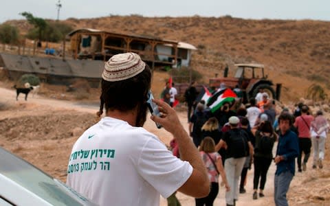 An Israeli settler speaks on the phone while Palestinian protesters and foreign activists enter a settlement outpost during a demonstration  - Credit: JAAFAR ASHTIYEH/AFP via Getty Images
