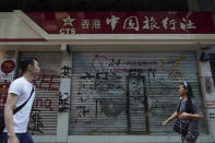 FILE - In this Oct. 7, 2019, file photo, pedestrians look at graffiti in front of China Travel Service in Hong Kong. Hong Kong’s embattled leader Carrie Lam said Tuesday that the city’s economy is being battered by months of increasingly violent protests. (AP Photo/Vincent Yu, File)