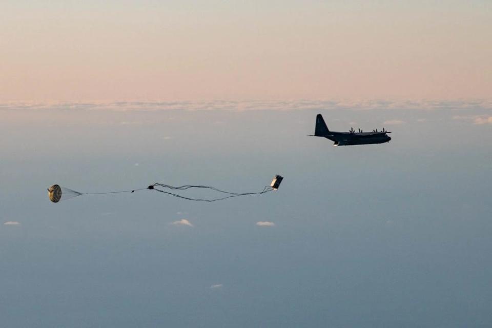 An MC-130J cargo plane drops a box attached to a parachute mid-flight.