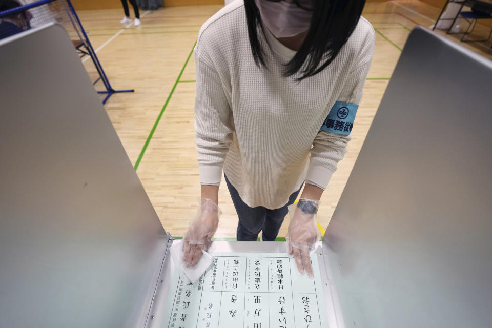 A staff member of a local election administration commission wearing a face mask disinfects one of the booths for voters in the lower house election at a polling station Sunday, Oct. 31, 2021, in Tokyo. (AP Photo/Eugene Hoshiko)