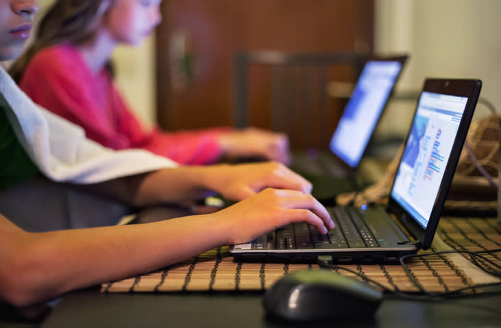 Two teens working on laptops, appearing focused on the task at hand