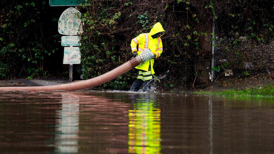 PHOTO: A worker carries a hose on a flooded street, on Feb. 1, 2024, in Long Beach, Calif.  (Eric Thayer/AP)