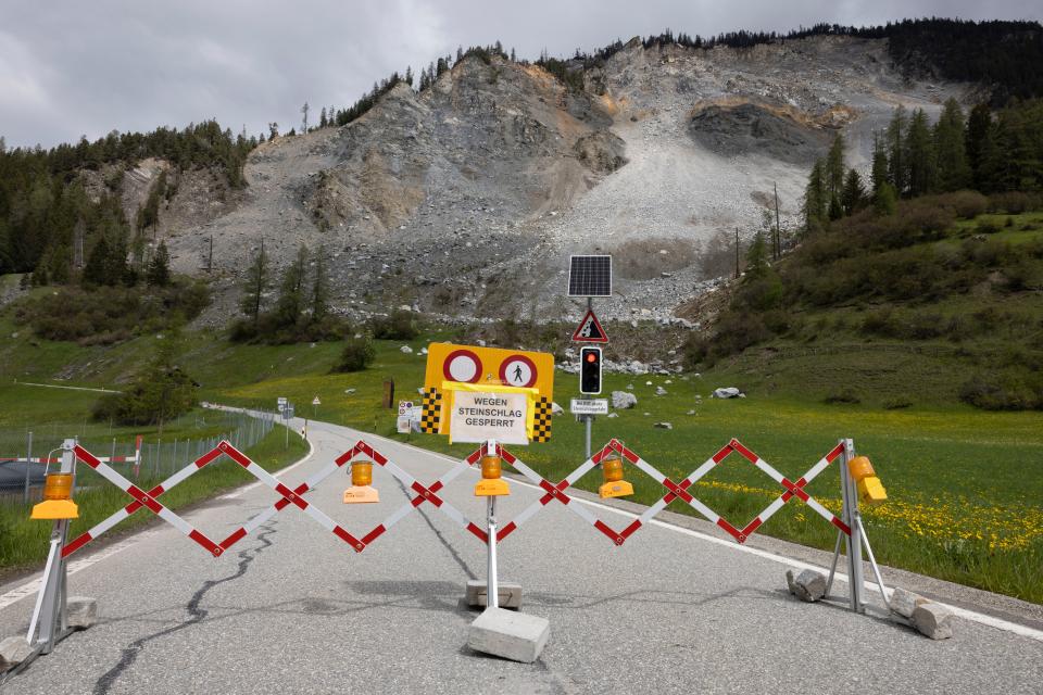 warning signs and fences block a road in front of a possible rockslide area in the mountains near Brienz-Brinzauls, Switzerland