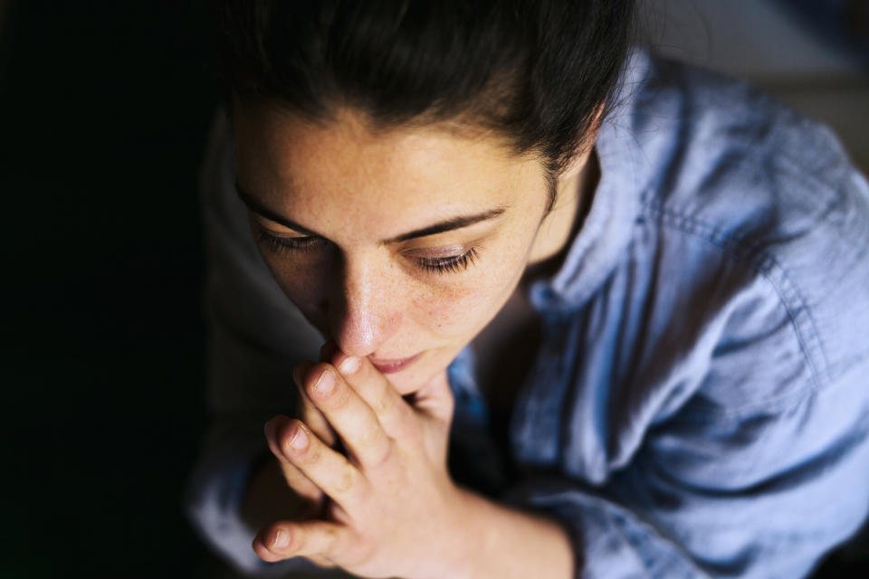 A person with closed eyes is resting their chin on their hands in a contemplative pose, wearing a casual button-up shirt