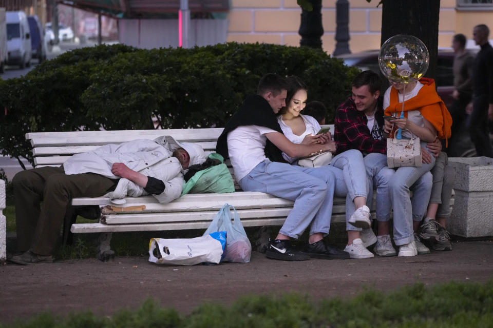 Young people sit in a park after the Scarlet Sails festivities marking school graduation in St. Petersburg, Russia, early Saturday, June 25, 2022. The Scarlet Sails celebration is a rite of passage both figuratively and literally. Every year, tall ships with glowing red sails make their way down the Neva River in St. Petersburg to honor recent school graduates as they set out on the journey into adulthood. (AP Photo/Dmitri Lovetsky)