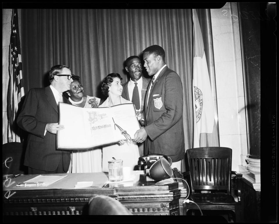 Rafer Johnson receives resolution from a man and a woman while his parents watch.